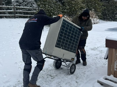 Two technicians moving a HVAC using in the snow.