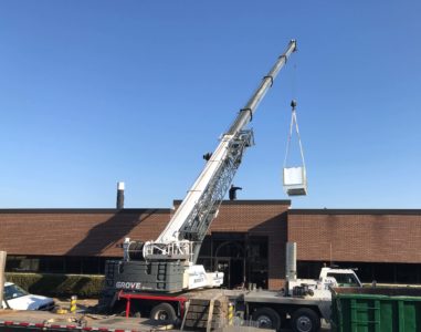 A crane lifting a commercial HVAC unit to the roof of a building.