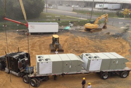 Commercial HVAC units being pulled by a large truck through a construction site.
