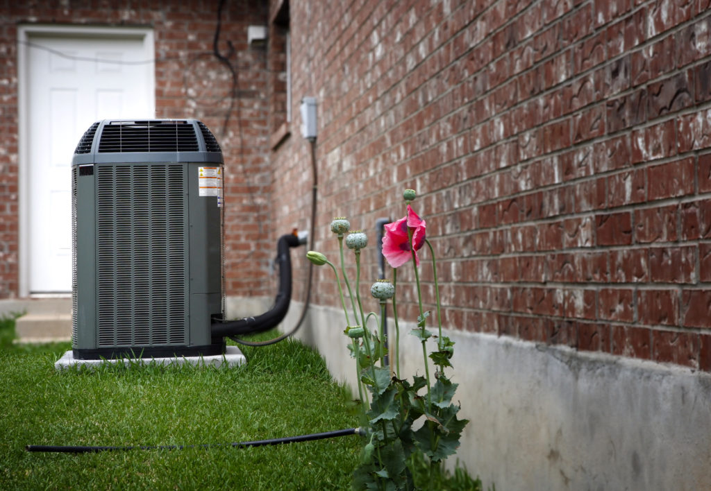Outdoor HVAC system beside brick house and spring flowers.